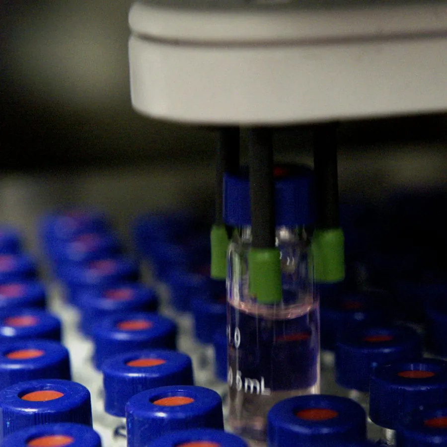Close-up of an HPLC autosampler gripper lifting a sample vial from a tray of blue-capped laboratory vials